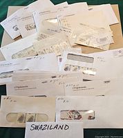 Photo showing multiple envelopes with windows revealing used postage stamps from Swaziland, each envelope labeled with issue numbers and markings.