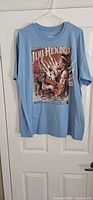 Full front view of the light blue Jimi Hendrix concert T-shirt hanging on a hanger from a door.