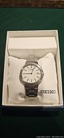 Top-front view of SEIKO men's wristwatch showing white dial with date in original box on cushion.