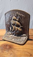 Front view of one cast brass sailing ship bookend showing detailed ship with three sails, arched top and wave-textured base.