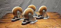Four wood and vinyl locking caster wheels mounted on metal brackets arranged on wood surface.