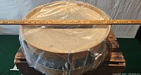 Top-down view of 15" snare drum in plastic wrap on wooden crate with ruler measuring diameter