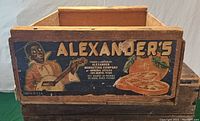 Side view of wooden crate showing colorful painted panel with Alexander's branding and cantaloupe graphics.