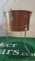 Side angle view showing wooden drum shell with green NEW ERA logo and chrome legs fully extended on green surface.