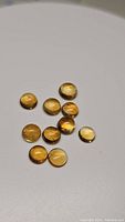 Eleven round cabochon cut golden citrine gemstones arranged loosely on a plain white surface showing their color, shape, and minor inclusions.