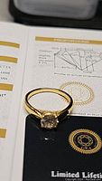 Photo showing the 18K gold electroplated ring with round brilliant cut moissanite set in sterling silver against a certificate background showcasing the certification graphics and diagrams.