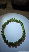 Photo of natural green jade bead bracelet under light showing bead color and shine.