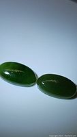Two oval deep green jade cabochon gemstones displayed flat on a white surface.