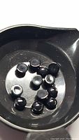 Close-up photo showing a collection of small round cabochon jet black onyx stones in a black container, highlighting their size, shape, and polished dome surfaces.