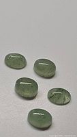 Five oval cabochon cut mint green kyanite gemstones with natural inclusions on a white surface.