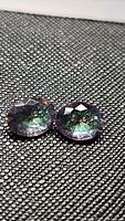 Close-up images of 2 oval cut Mystic Topaz gemstones lying on textured black surface, showing their rainbow purple tone and faceted tops.