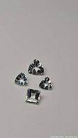 Three triangular trillion cut and one square princess cut aquamarine gemstones on gray background