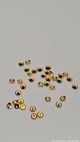 Multiple small round yellow Ceylon sapphire gemstones with diamond cut scattered on a light surface, showing size and color.