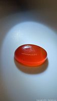 Photo of natural oval carnelian cabochon gemstone showing the deep orange translucent color and polished smooth surface.