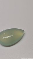 Pear-shaped natural chalcedony gemstone cabochon showing smooth polished surface and teal blue coloration under white lighting.