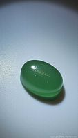 Oval green aventurine cabochon gemstone with smooth polished surface, shown from an angle to reveal translucency and color depth.