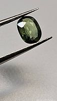 Close-up photo of one oval cut natural green sapphire held with tweezers showing the gem's facets and color.