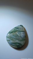 Pear-shaped polished natural moss agate cabochon gemstone showing green moss-like inclusions and small surface imperfections.