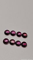 Lot of eight round cabochon pink sapphires arranged on a grey background, showing color and size.