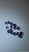 Group of 18 natural purple iolite round cabochon stones arranged on a neutral background, showing smooth polished surfaces and deep purple color.