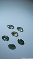 Six green oval faceted stones on white background under neutral light