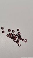 Multiple small round rhodolite garnet gemstones arranged loosely on a flat surface, showing reddish-purple color and transparent polished finish.