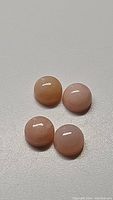 Four small round pink opal gemstones arranged on a plain surface. They are smooth, glossy, and show a soft pink color.