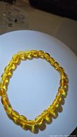 Photo showing the natural golden translucent amber beads arranged in a stretchy bracelet on a white curved surface.