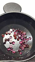 Multiple small round cabochon rhodolite garnet gemstones in a black container, showing color range and size.