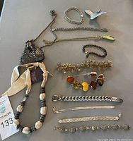 Full view of all thirteen jewelry pieces arranged on a surface, showing bracelets, necklace, bird pendant and silver mesh purse.