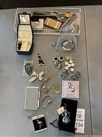 Full lot view showing many pieces including earring pairs, pins, charms, brooches, wristwatch and notebook with pen