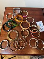 Overview of all 20 bracelets displayed on wood surface showing variety in color and material including 4 lucite or bakelite pieces.