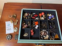 Assorted earrings and brooches in black dividers open box showing many pairs of earrings including studs and clip-ons in various colors