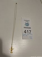 Full view of gold chain and pendant laid flat next to auction label