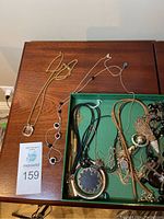 Image of the lot on wooden surface including multiple necklaces and a box with additional jewelry, highlighting the variety of styles and materials.