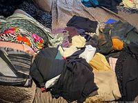 Photo of a large pile of scarves in various colors and patterns spread on bedding, showing the diversity and quantity