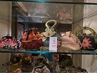 Five embellished clutch purses displayed on glass shelf: one Vera Bradley floral embroidered clutch and four Mary Frances beaded novelty clutches
