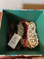Top view of square box showing multiple necklaces tightly packed, including white, black, red, clear, and brown beads.