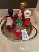 Seven assorted decorative glass perfume bottles displayed on a round mirrored metal tray on a bathroom counter.