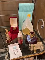 Five perfume bottles displayed on glass table including boxed Kenzo Parfum d'ete and ornate bottles