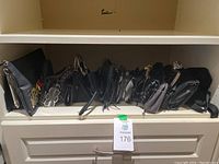 Photo showing 19 purses lined up in a row on a shelf, mostly black or dark colors, evening style purses with various shapes and chain or strap handles.