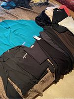 Full view of assorted sweaters and pants including a bright turquoise sweater and dark colored clothing pieces.