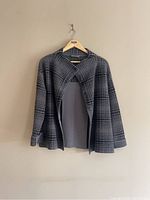 Charcoal grey check open-front jacket on wooden hanger against beige wall
