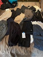 Overview photo showing 19 sweaters laid out on bed in various neutral colors including black, beige, cream, navy, and grey. Some have button details.