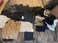 Photo showing multiple black, white, and beige sleeveless tops with glitter and textured patterns, laid out on bed.