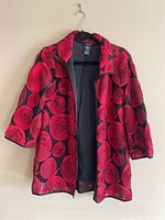 Red and black jacket with rose print, mid-length silhouette on black hanger against wall