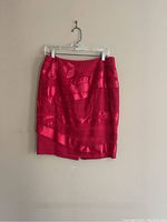 Bright red skirt on clear hanger against wall showing horizontal pattern.
