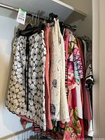 Multiple garments on rack including black and white floral skirt, coral skirt, lace skirt and printed tops behind