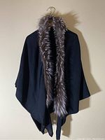 Black knit shawl with a grey fur-trimmed collar draped on a hanger