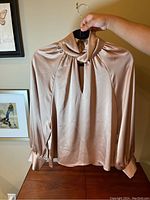 Beige satin blouse with draped collar and keyhole front hung on hanger